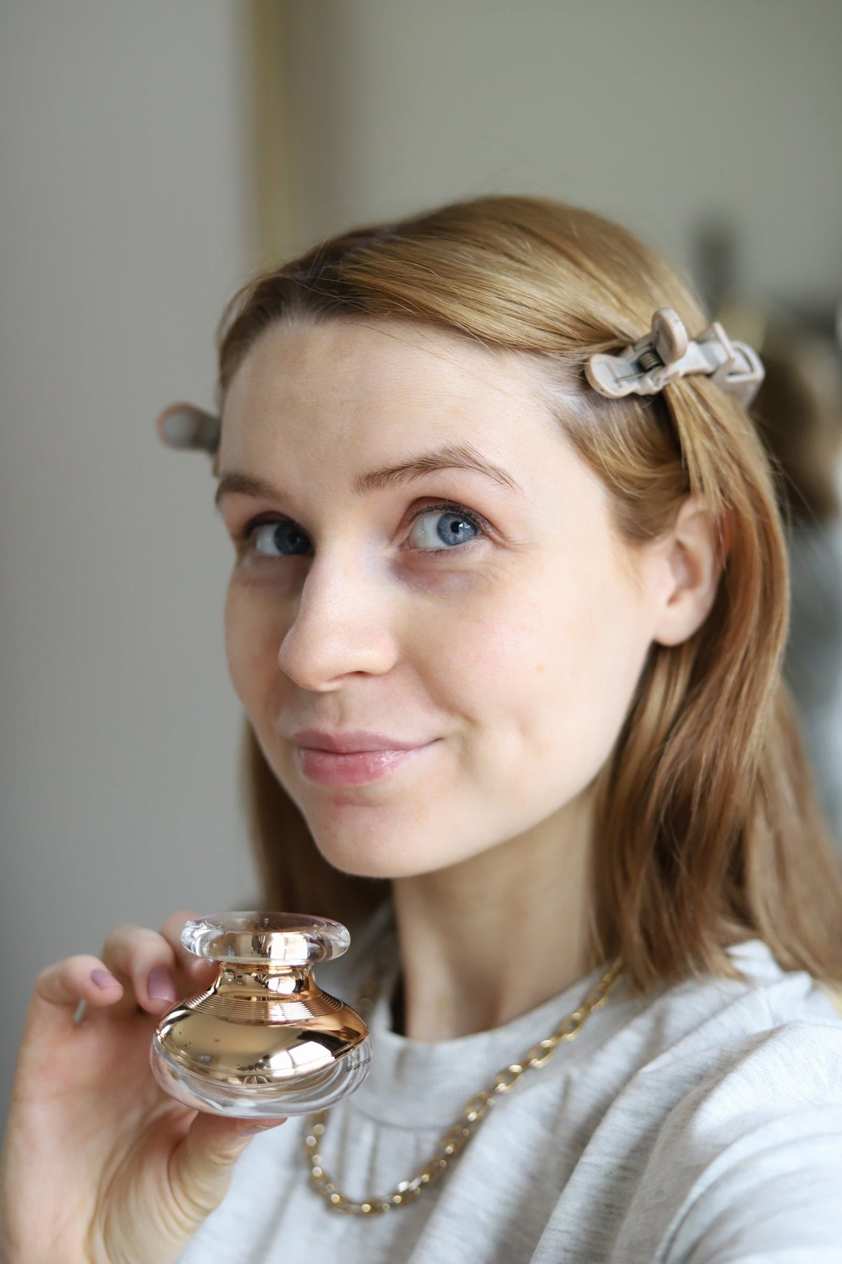 Close-up of a woman with a hair clip holding the EpiLynx eye cream jar near her chin