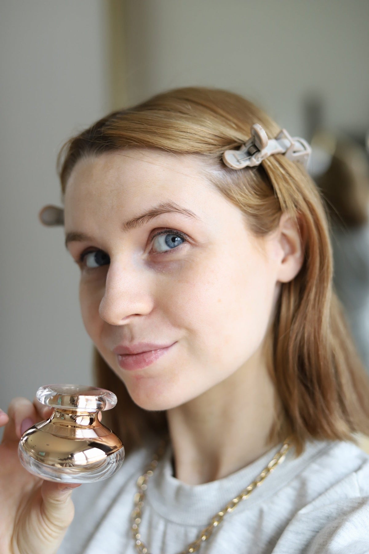 Woman with a hair clip holding the EpiLynx eye cream jar up beside her face