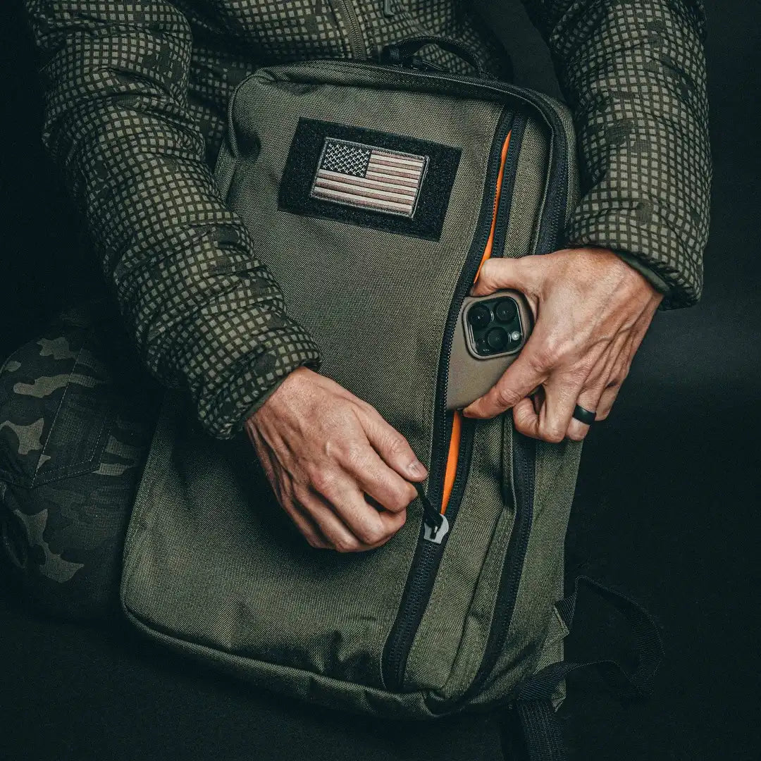 Hands opening the front zipper pocket of the olive green Recycled Firefighter 24 Hour Backpack