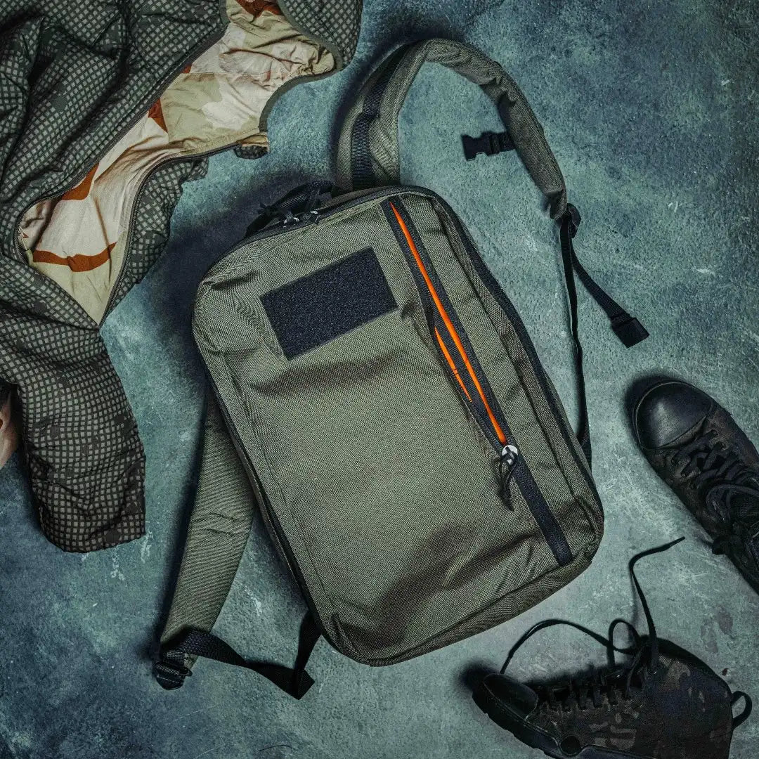 Olive green Recycled Firefighter 24 Hour Backpack lying on a teal surface next to a boot and clothing