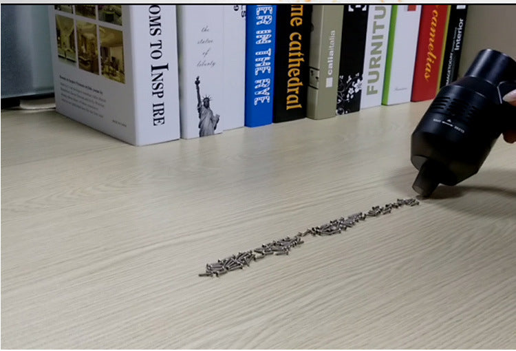 Mini vacuum cleaning a line of debris on a light desk in front of books