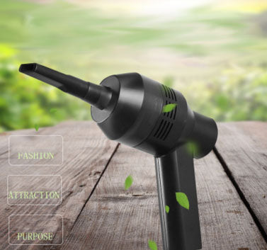 Black mini vacuum cleaning dust on a wooden table with green leaves in the background