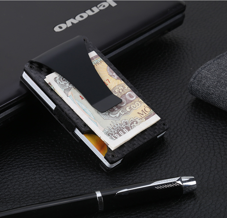 MagShield card holder with banknotes tucked in its metal money clip, beside a pen on a dark laptop