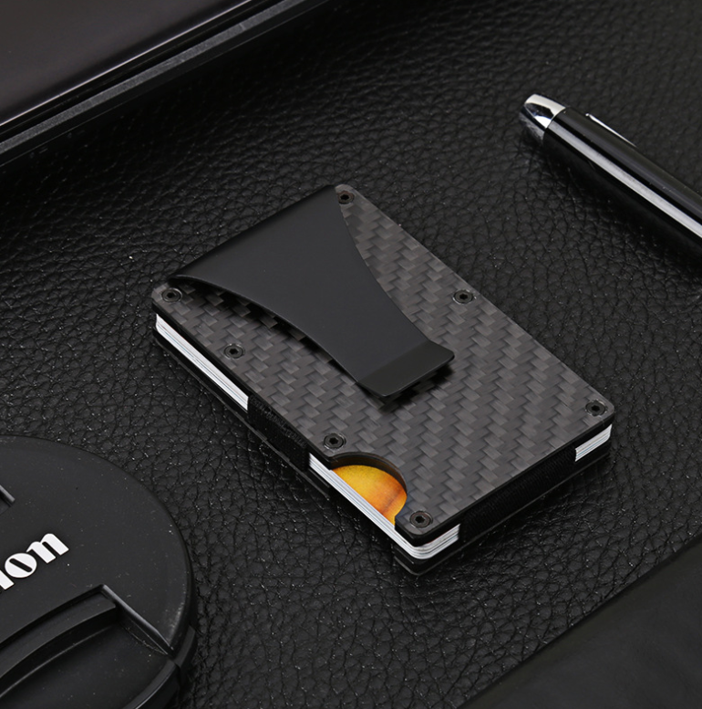 MagShield card holder with a metal clip lying on a dark laptop beside a pen