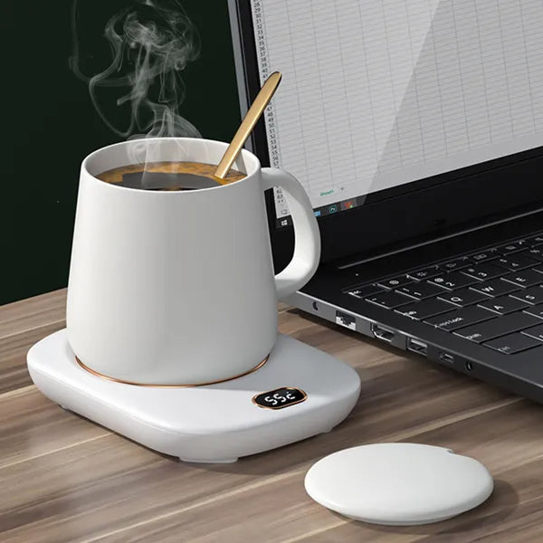 White mug warmer with a steaming cup on a desk beside a laptop
