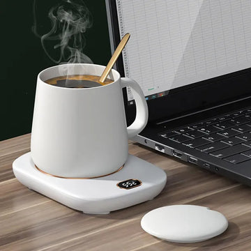 White mug warmer with a steaming cup on a desk beside a laptop
