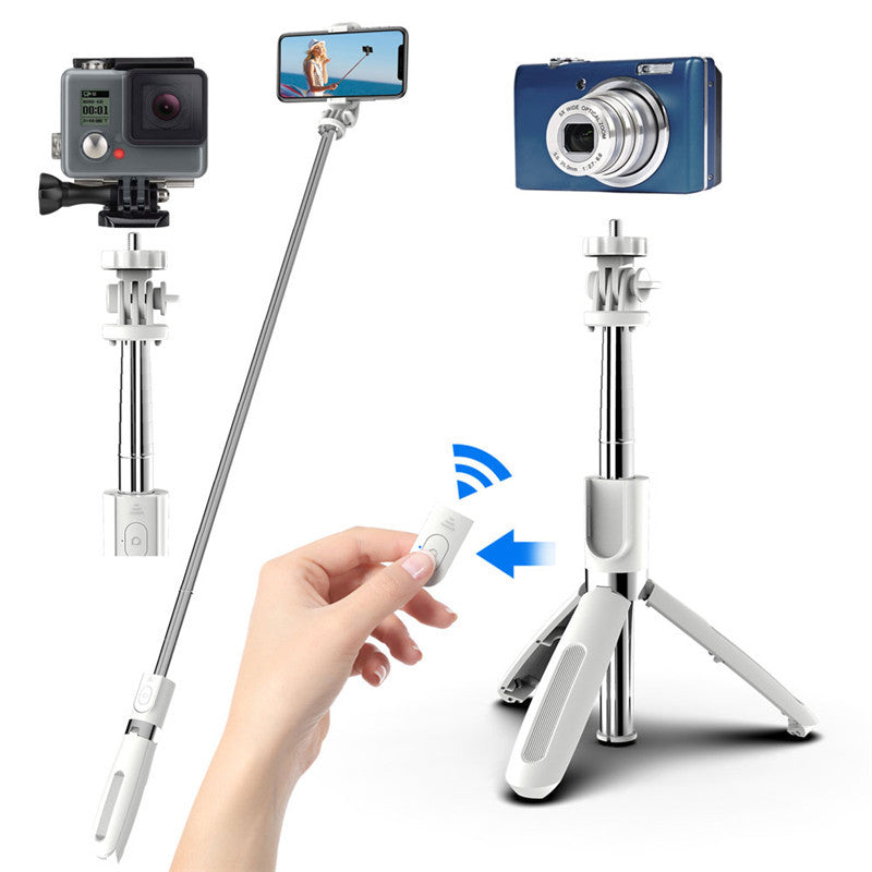 White Bluetooth selfie stick tripod holding a phone, beside a tripod with a compact camera and a hand holding the remote