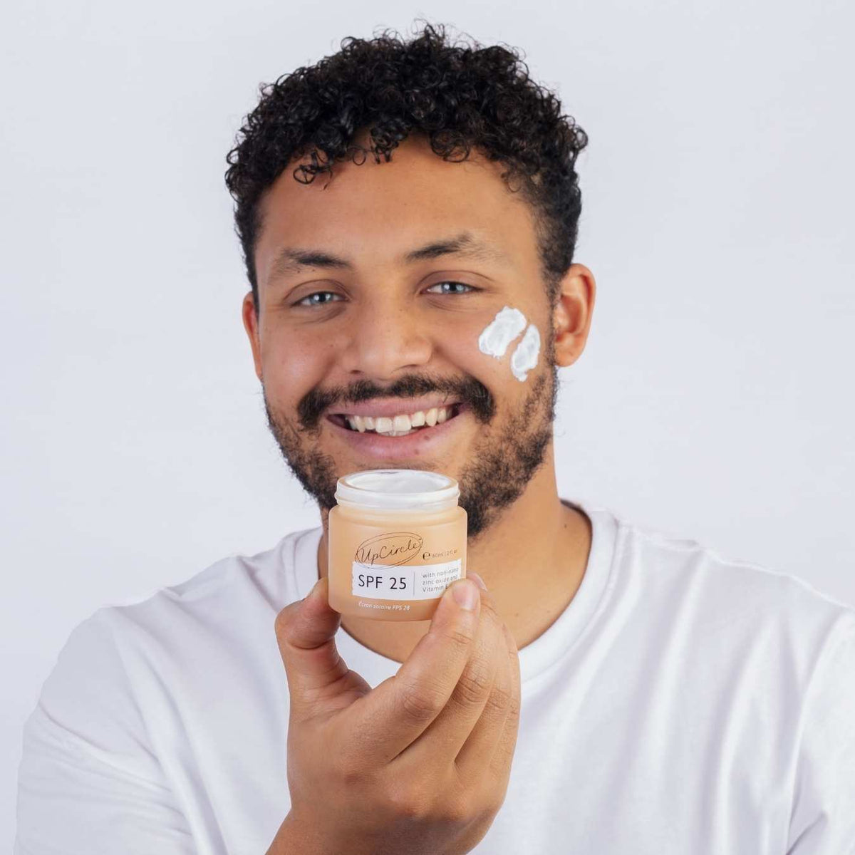 Smiling man holding an UpCircle balm jar with a dab of balm on his cheek