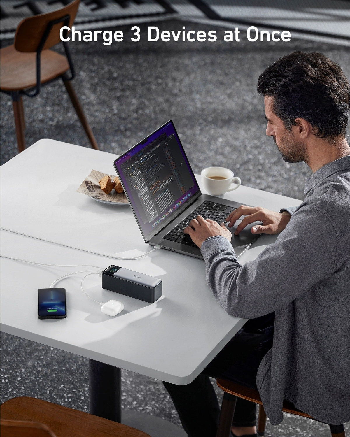 Man working on a laptop at a table while the power bank charges three devices, with the text Charge 3 Devices at Once