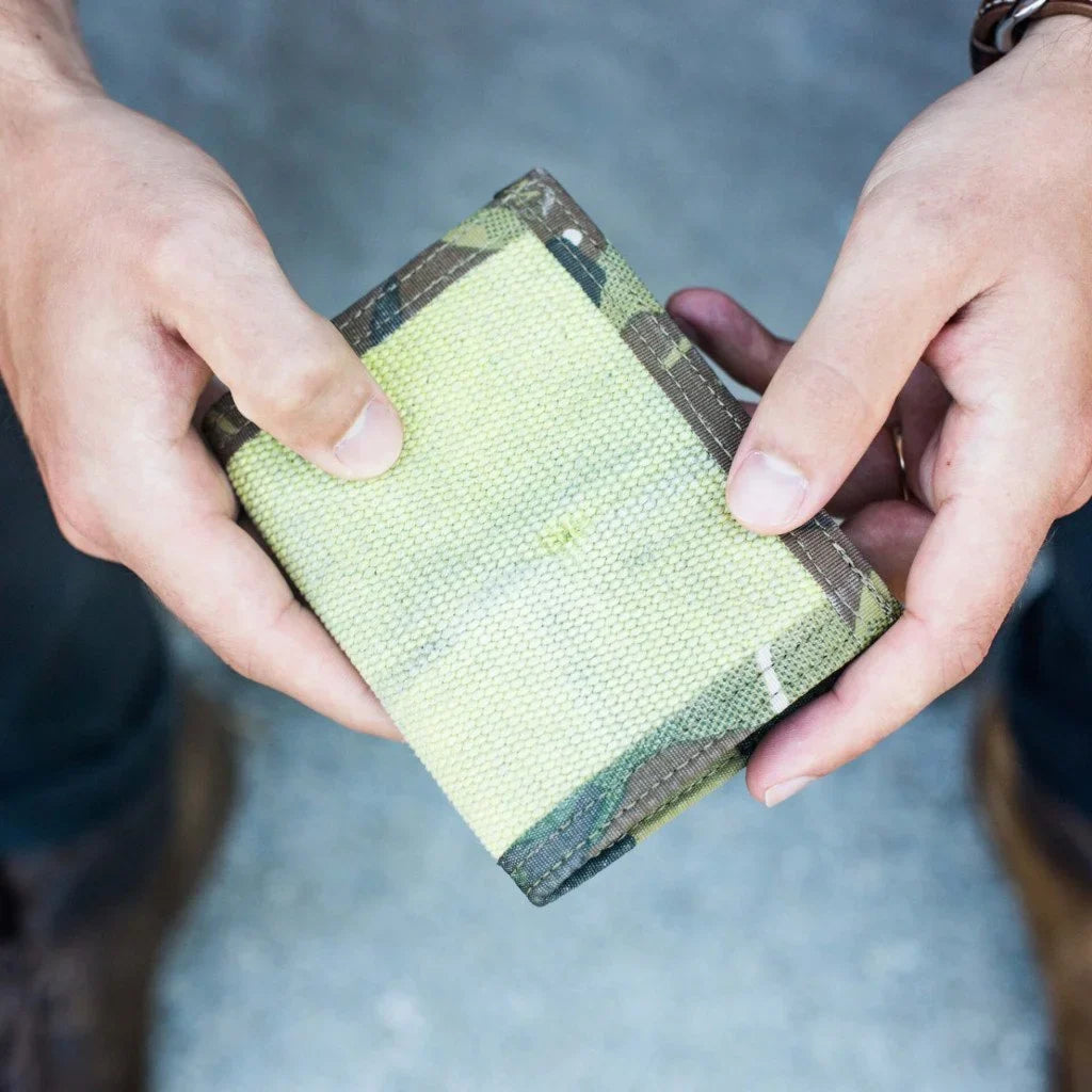 Hands holding a pale yellow-green fire hose wallet with camouflage trim