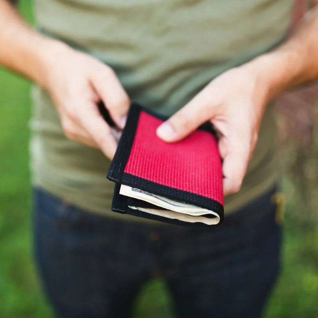 Person in an olive shirt holding a red fire hose wallet with cash inside
