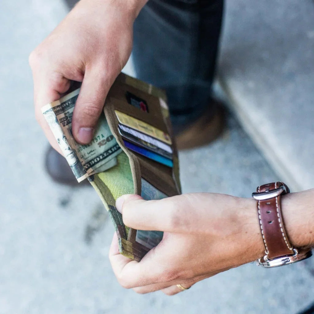 Hand pulling cash and cards from a tan wallet, with a watch on the wrist