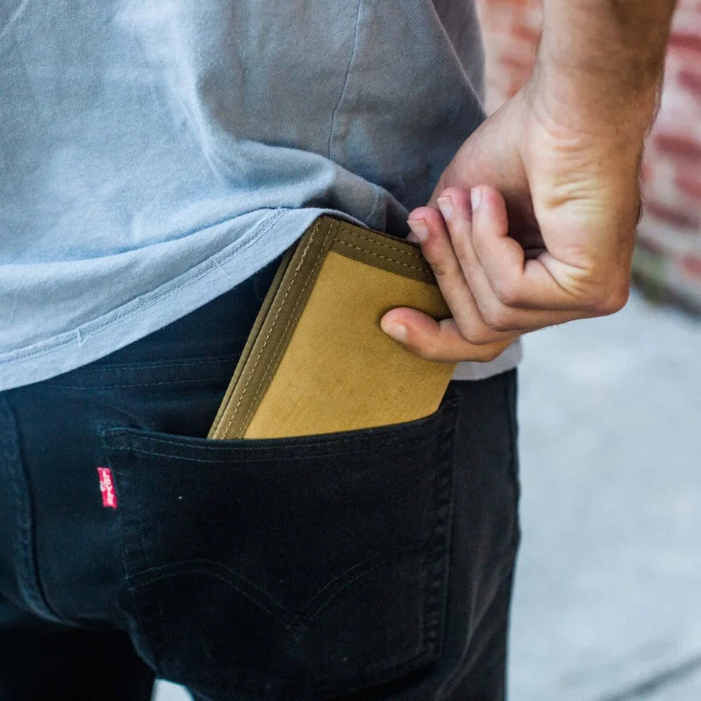 Man in a gray shirt sliding a tan wallet into the back pocket of black jeans