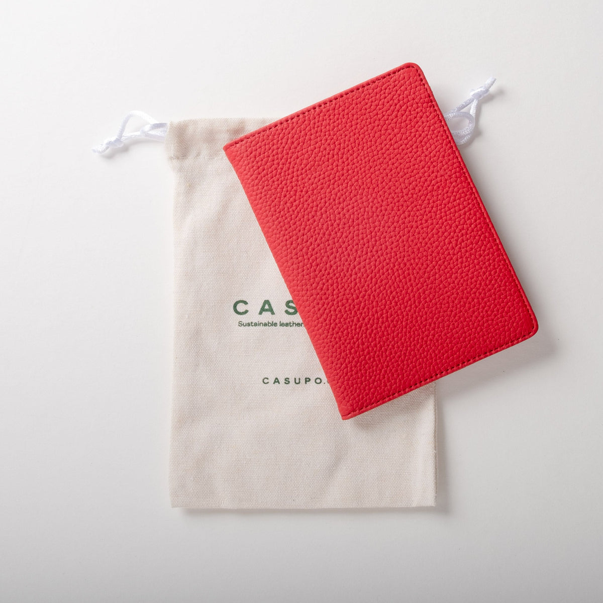 Red passport wallet beside a cream CASUPO drawstring pouch