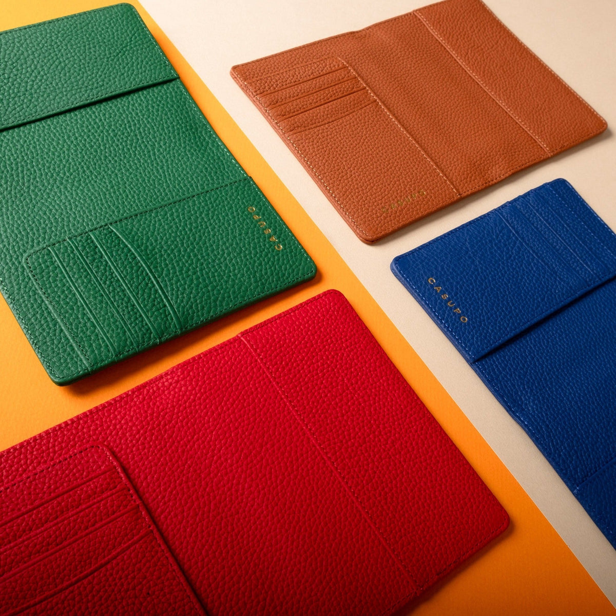 CASUPO passport wallets in green, tan, red and cobalt blue shown open on an orange and cream surface