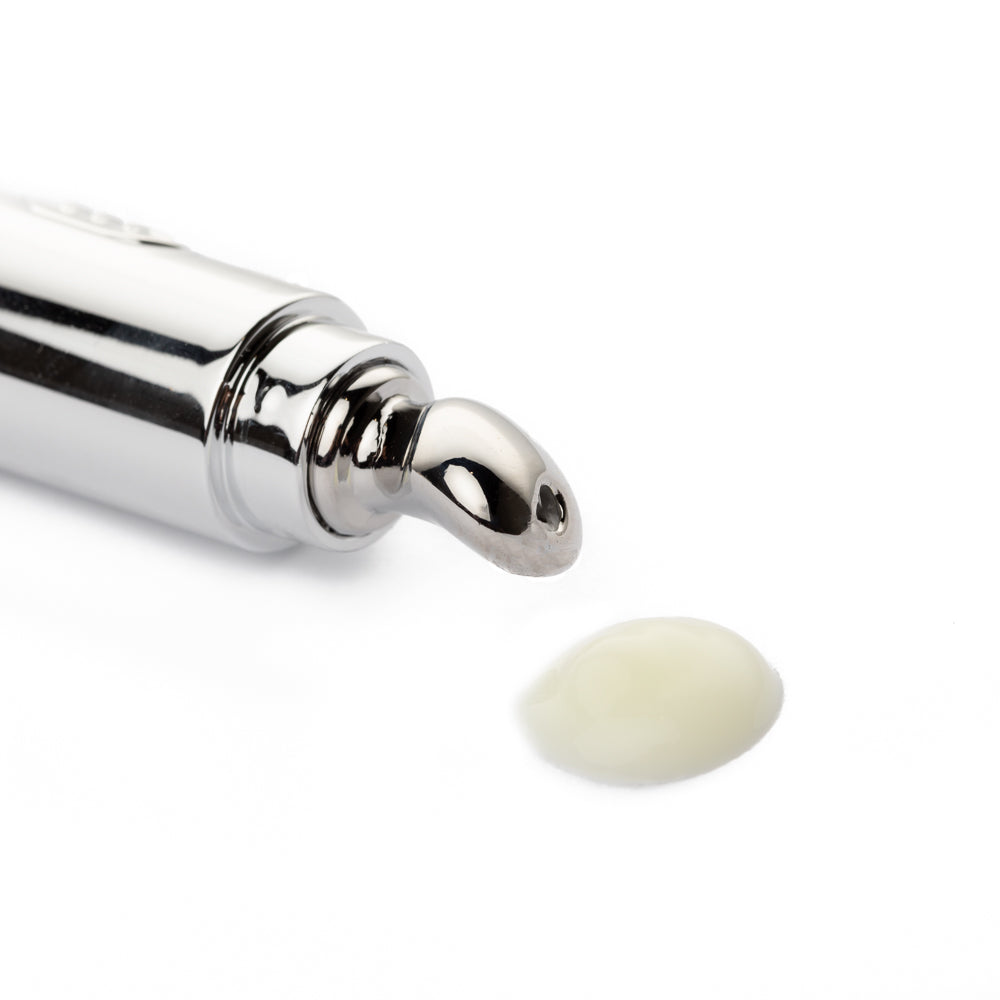 Silver eye cream applicator tube with a dab of cream beside it