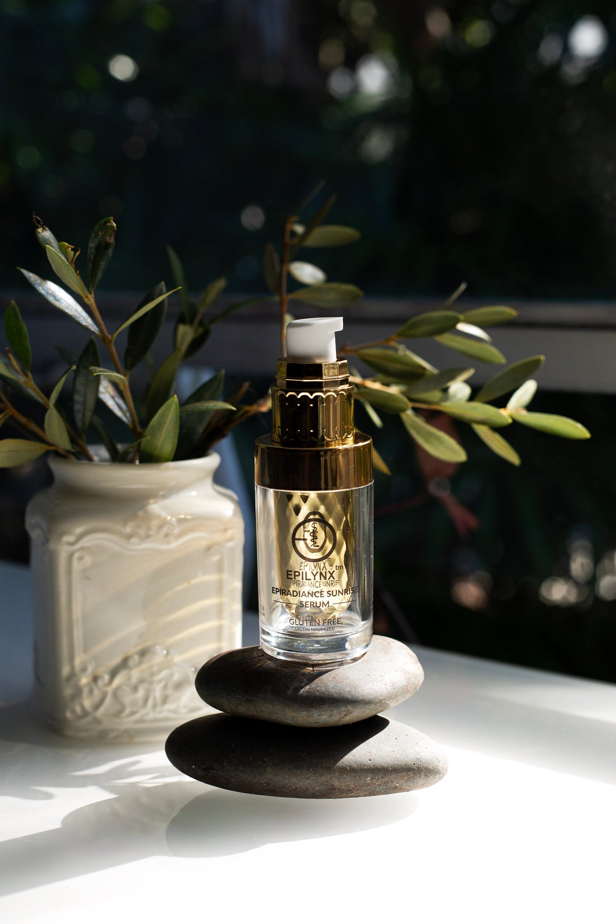 Gold serum bottle on a ledge beside a plant and stacked stones