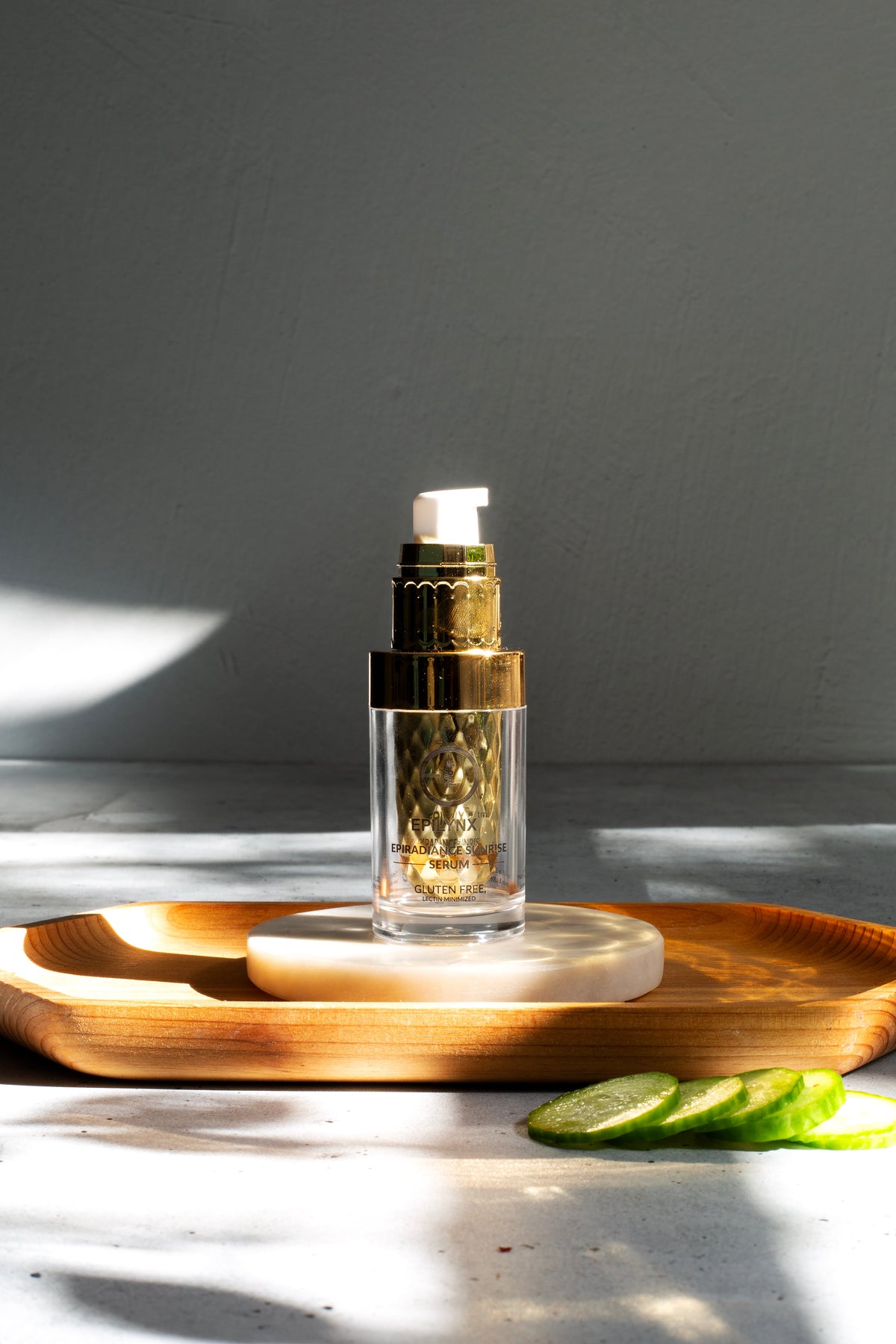 Gold serum bottle on a wooden tray with cucumber slices in bright light