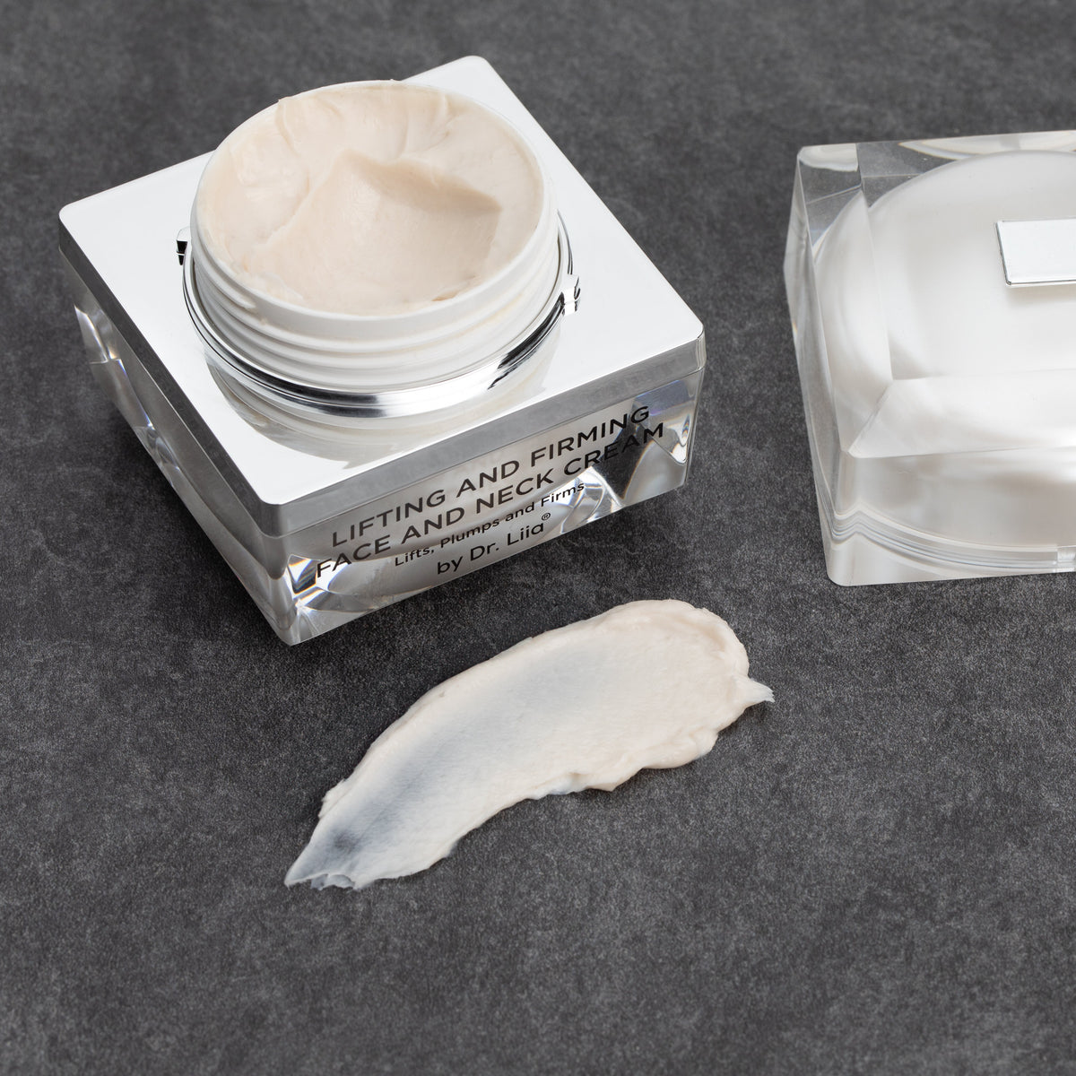 Open cream jar beside its lid and a smear of cream on a dark surface