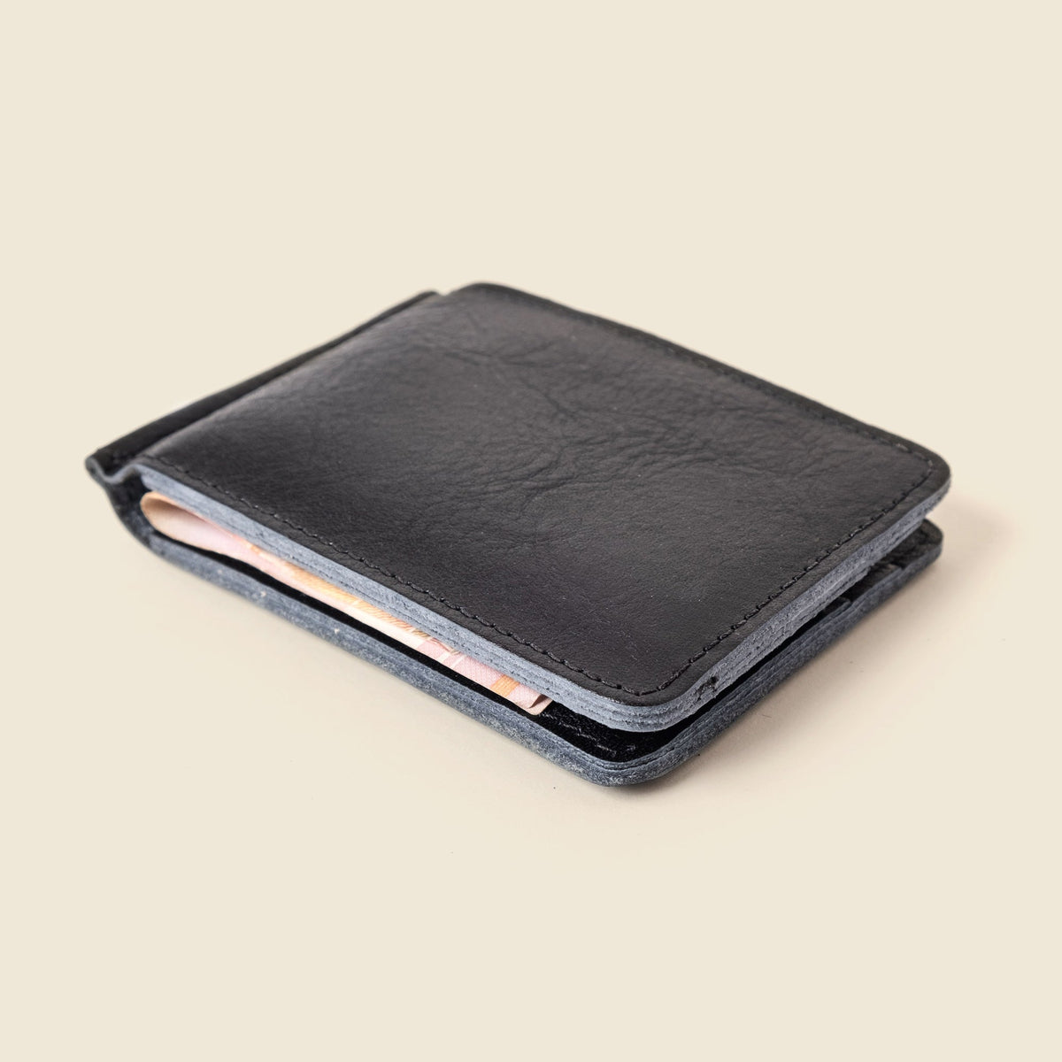 Black leather money clip wallet at an angle with cash tucked inside