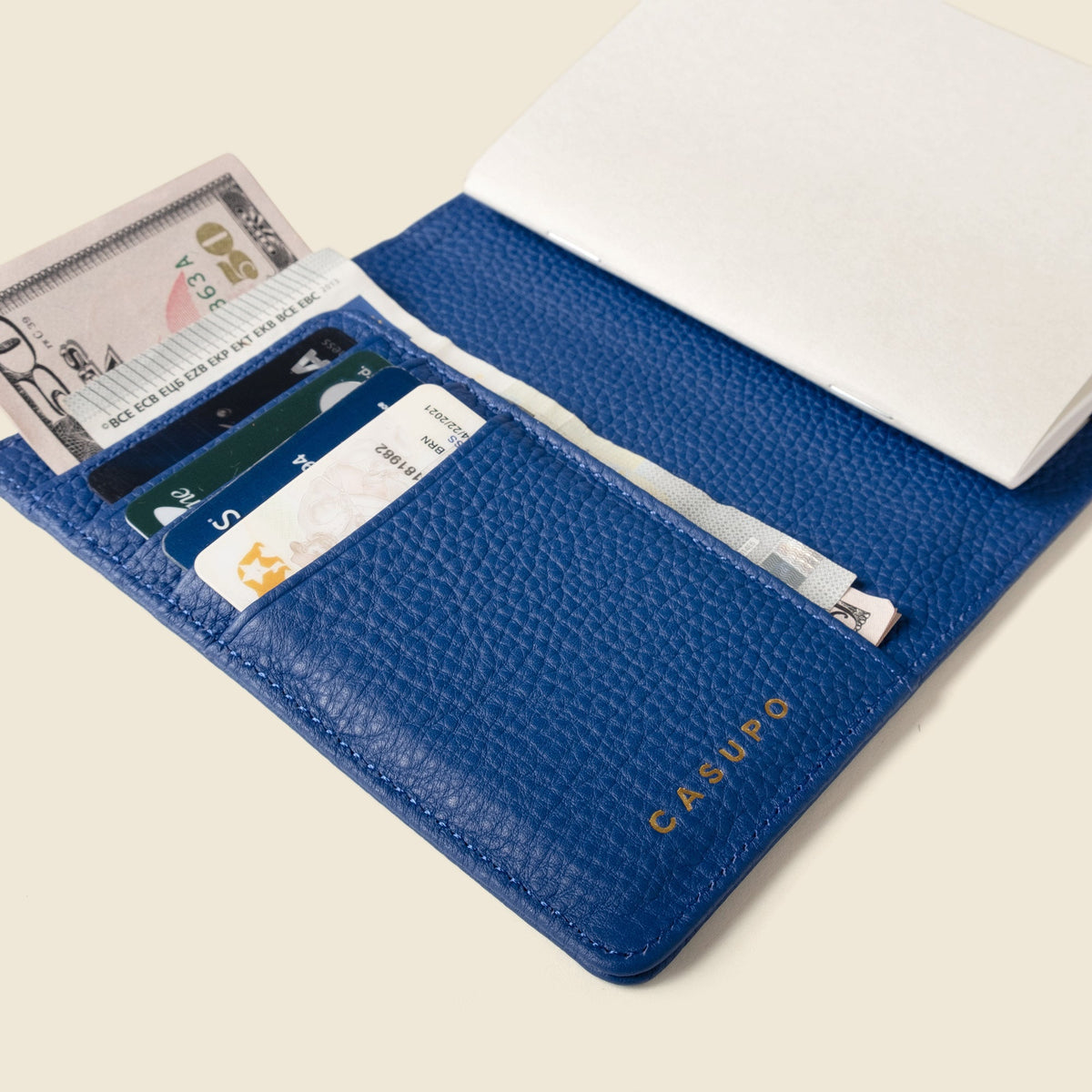 Open cobalt blue passport wallet with cards, a boarding pass and cash tucked in, beside a notebook