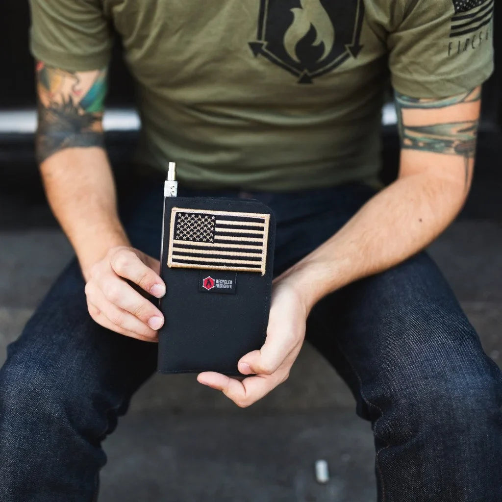 Seated man in a green T-shirt and jeans holding the black Field Notes Wallet with a US flag patch