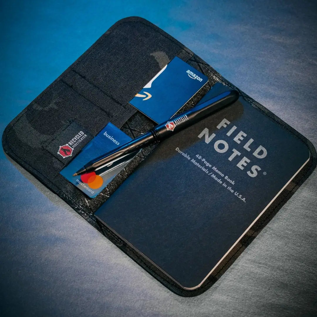 Open black multicam Field Notes Wallet with a notebook and several cards on a dark blue surface