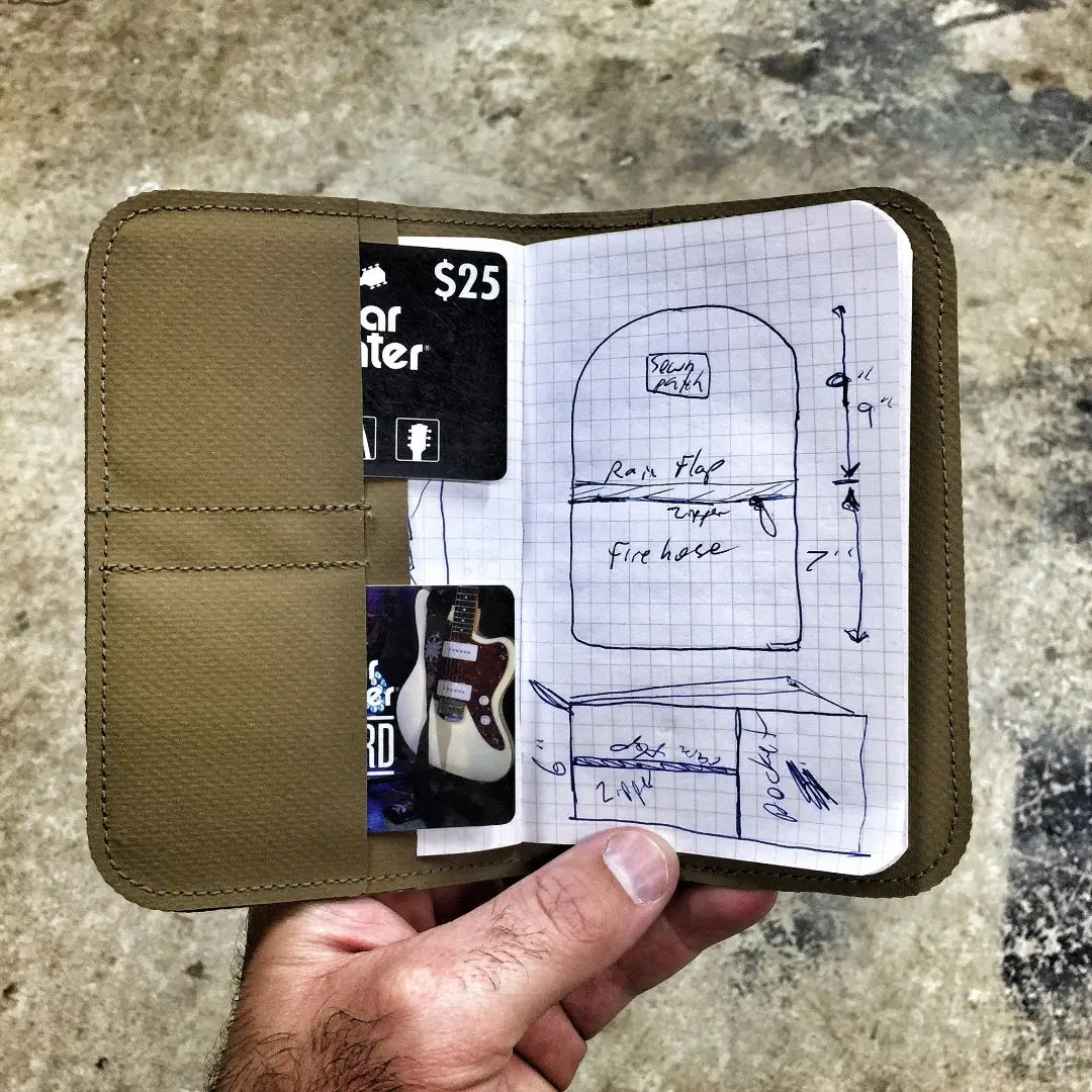 Hand holding the open Field Notes Wallet with a notebook page of handwritten sketches and a card in the side pocket