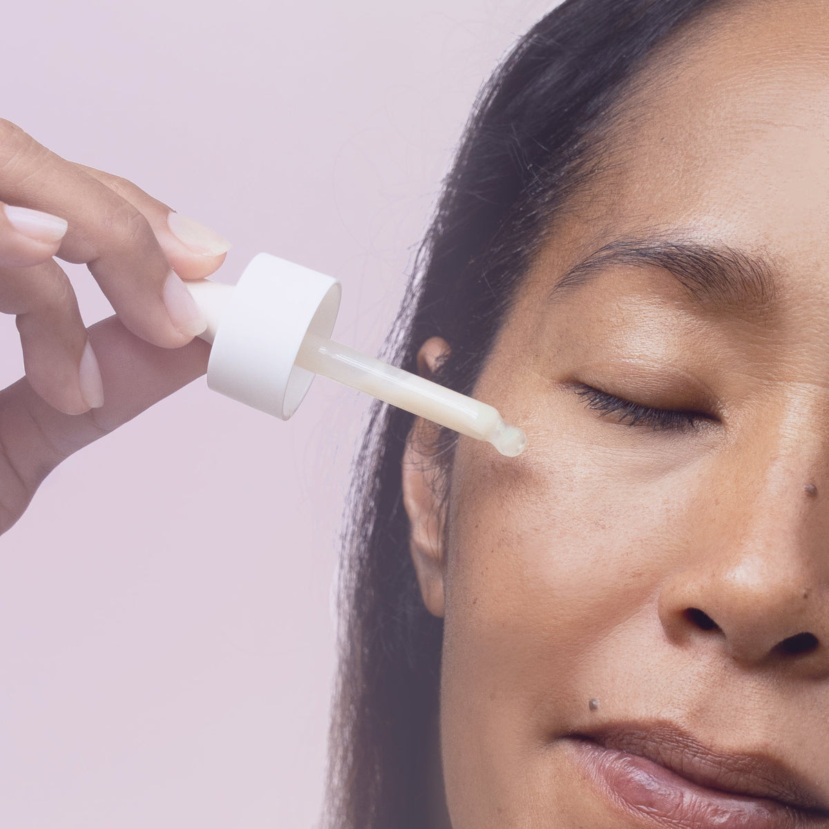 Close-up of a woman's face as a dropper applies serum to her cheek