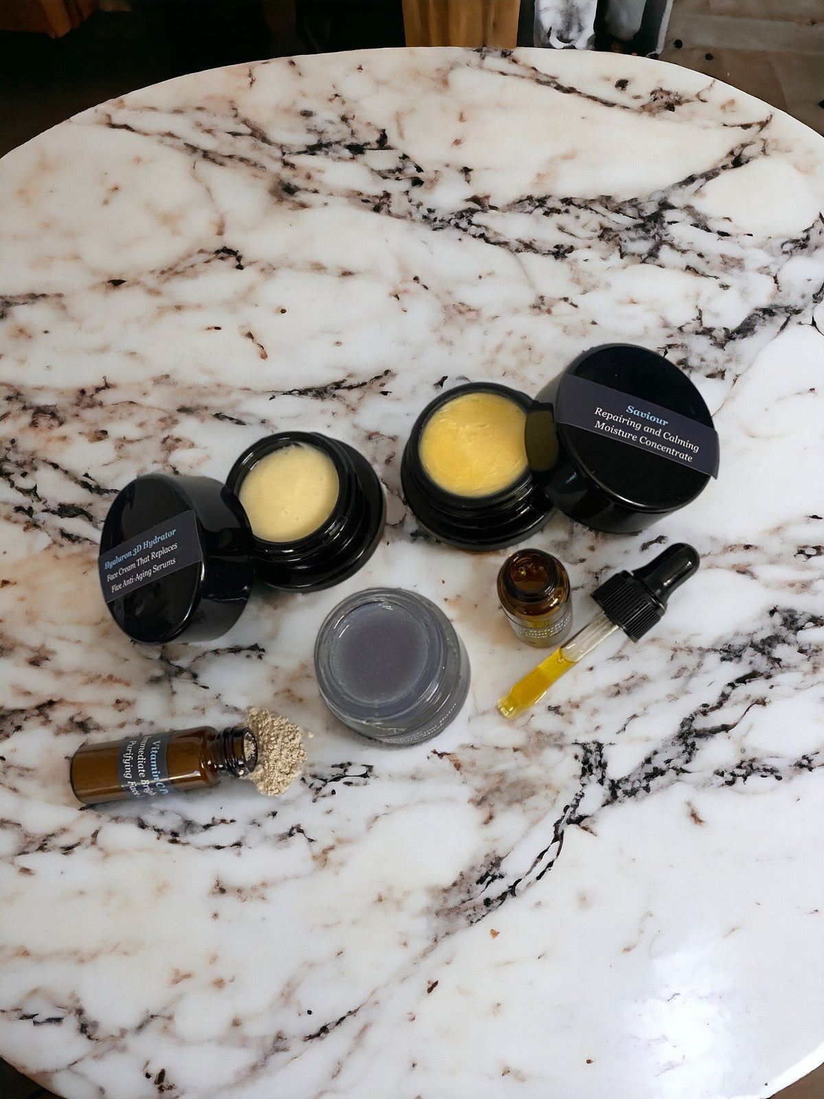 Open jars of yellow balm and cream with a dropper and vials on white marble