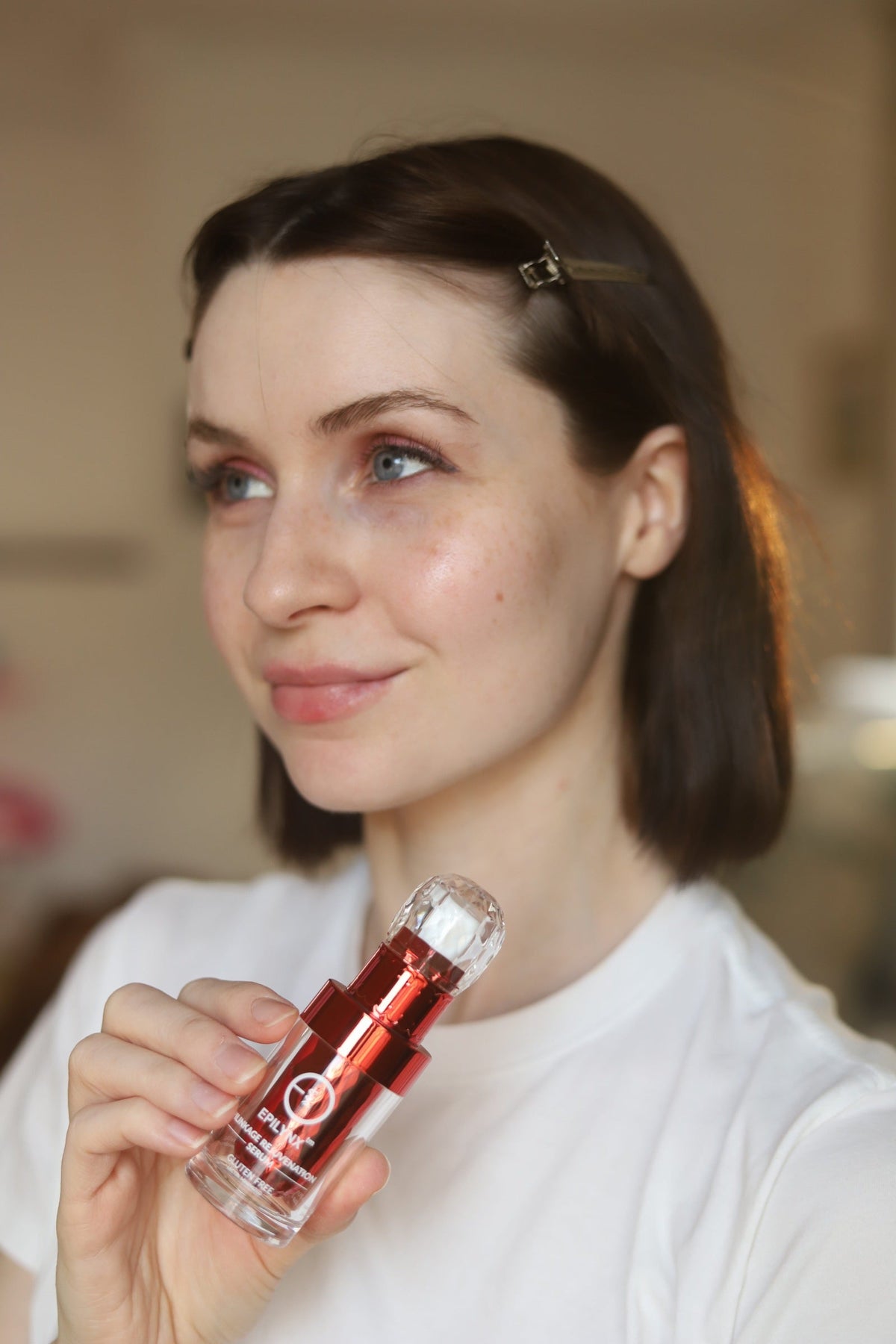 Woman in a white T-shirt holding a small red serum bottle