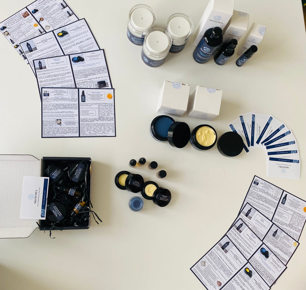 Flat lay of NILCEUTICA jars, bottles and instruction cards scattered on a cream surface