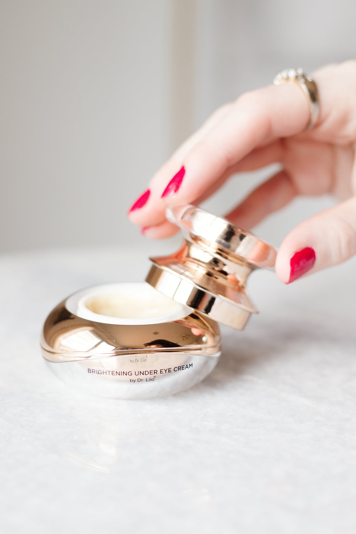 Hand with red nails opening the gold EpiLynx eye cream jar on a white surface