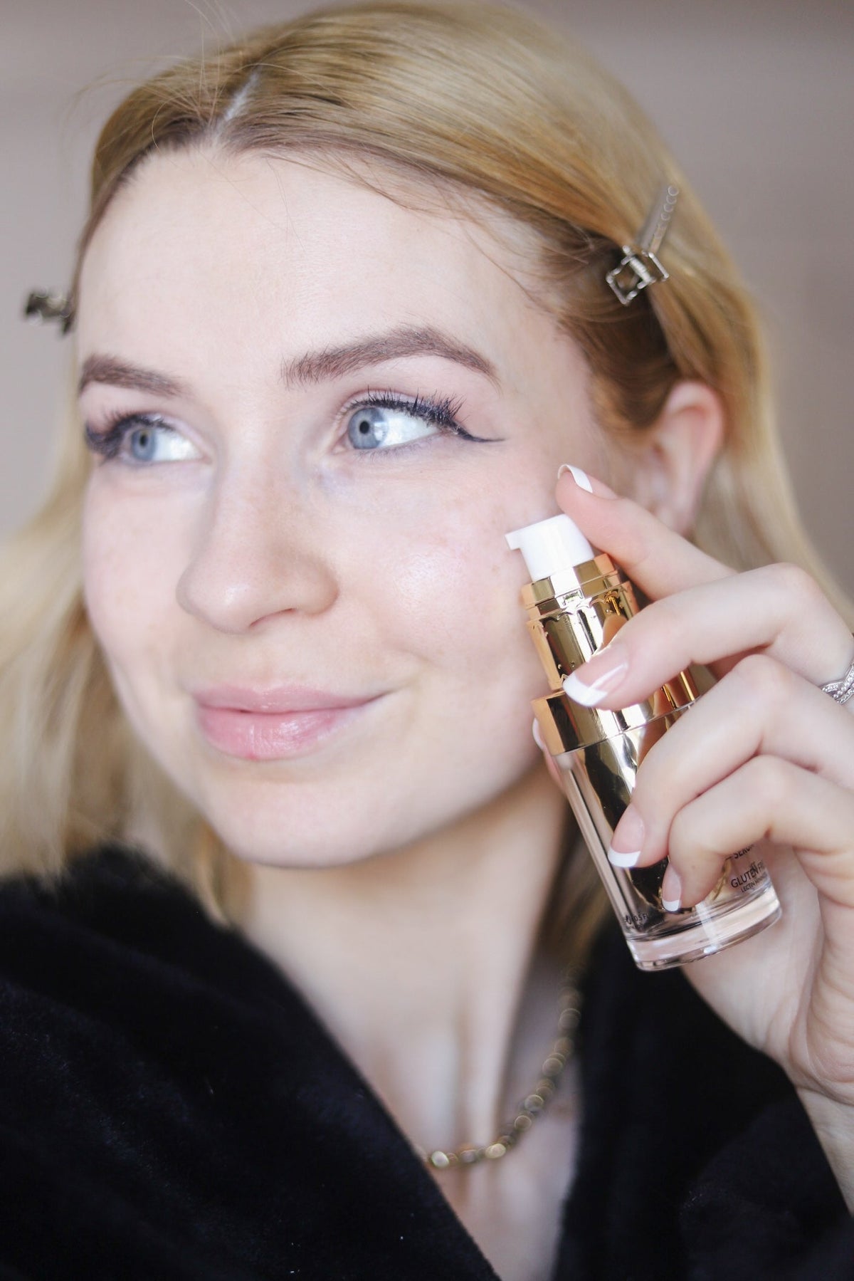 Woman in a black robe holding the gold serum bottle to her cheek