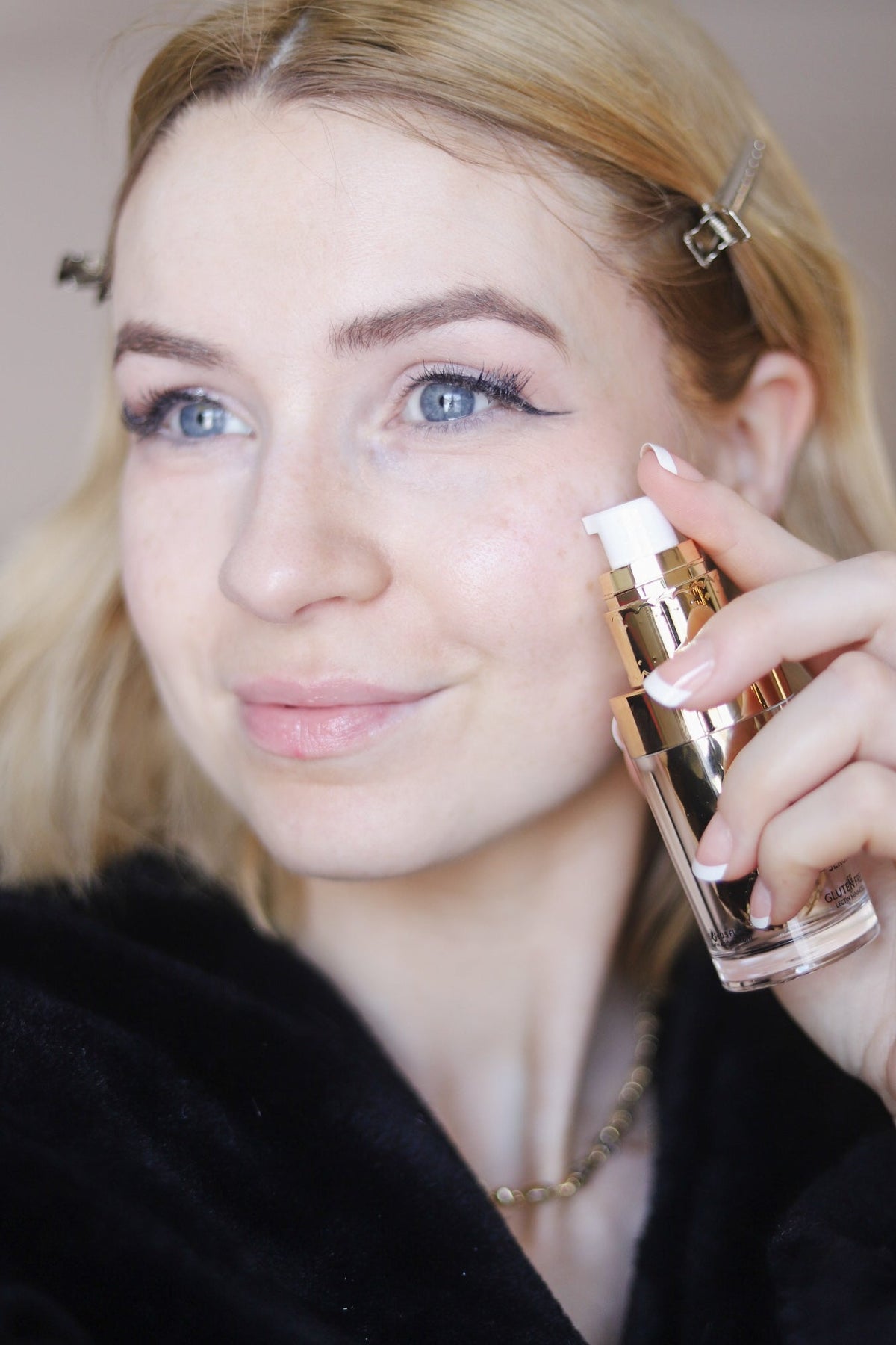 Woman in a black robe holding the gold serum bottle near her face