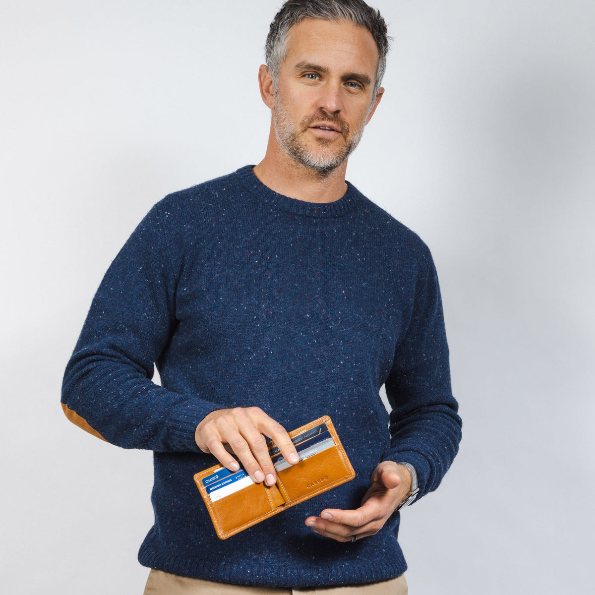 Man in a navy sweater holding the open tan leather billfold with cards showing in the slots