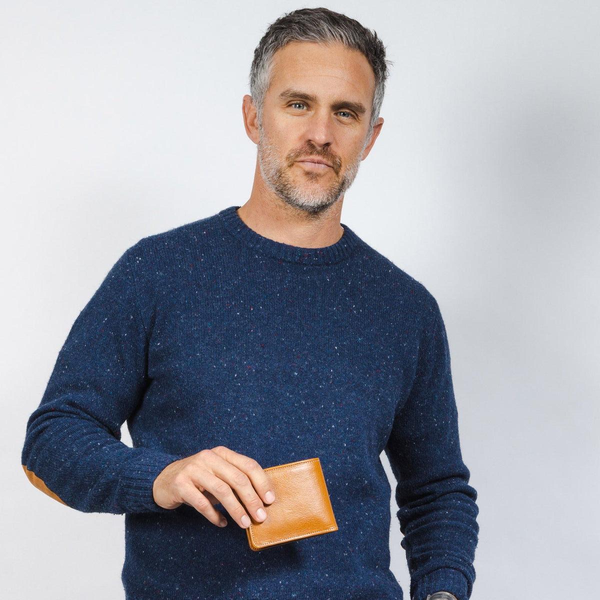 Man in a navy sweater holding a small tan leather wallet