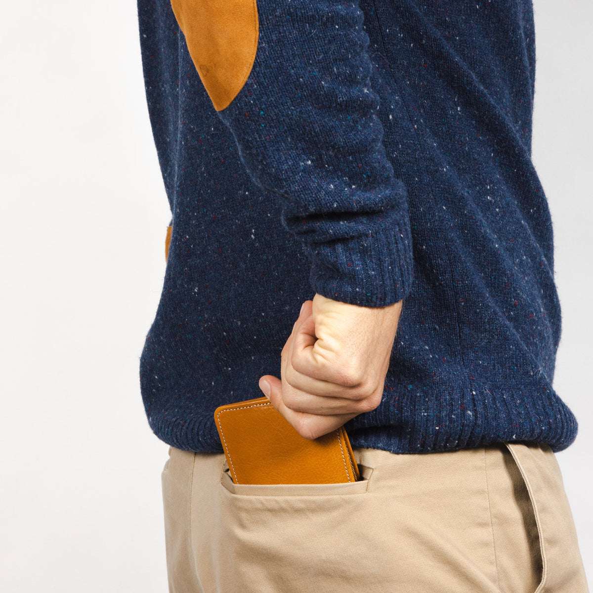 Man in a navy sweater and khakis sliding the tan leather wallet into his back pocket