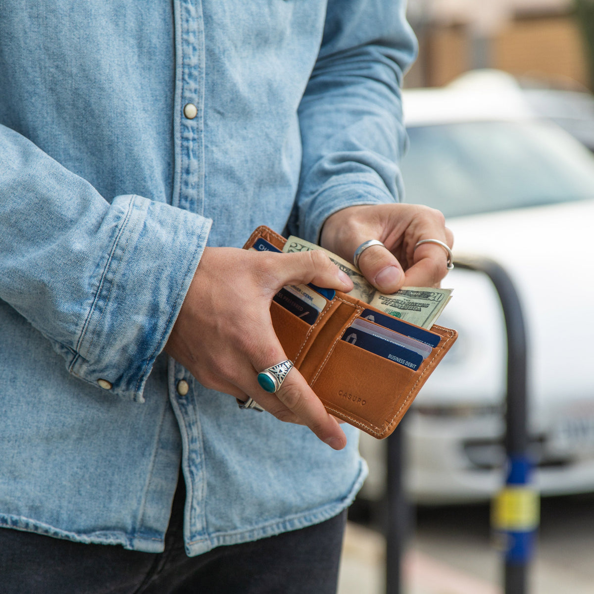 Man in a denim shirt holding the open tan leather billfold with cash and cards