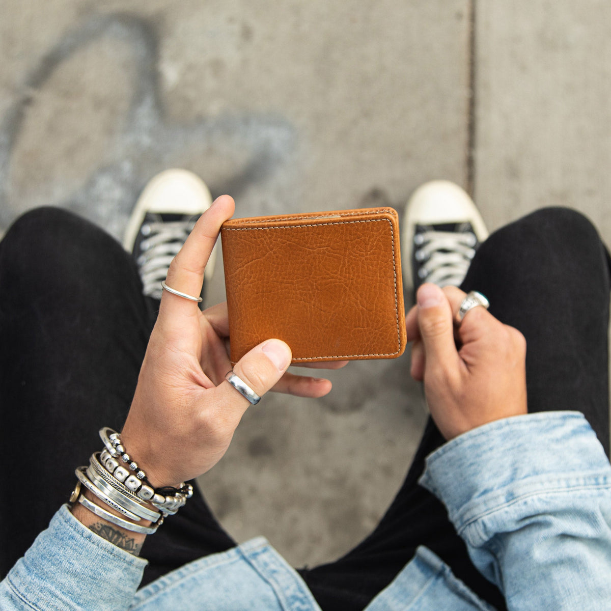 Person looking down at the tan leather billfold held in both hands, sneakers visible on the pavement