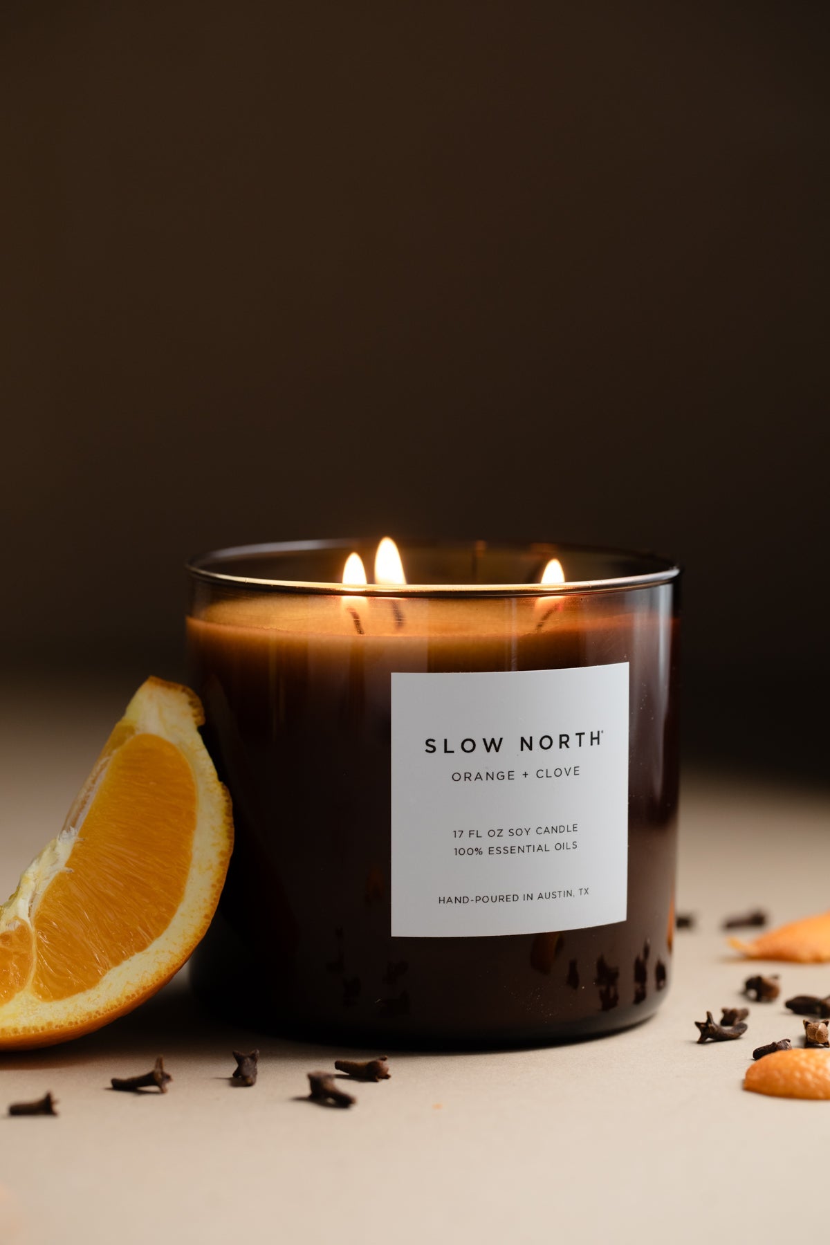 Lit candle in an amber jar beside an orange slice in low light