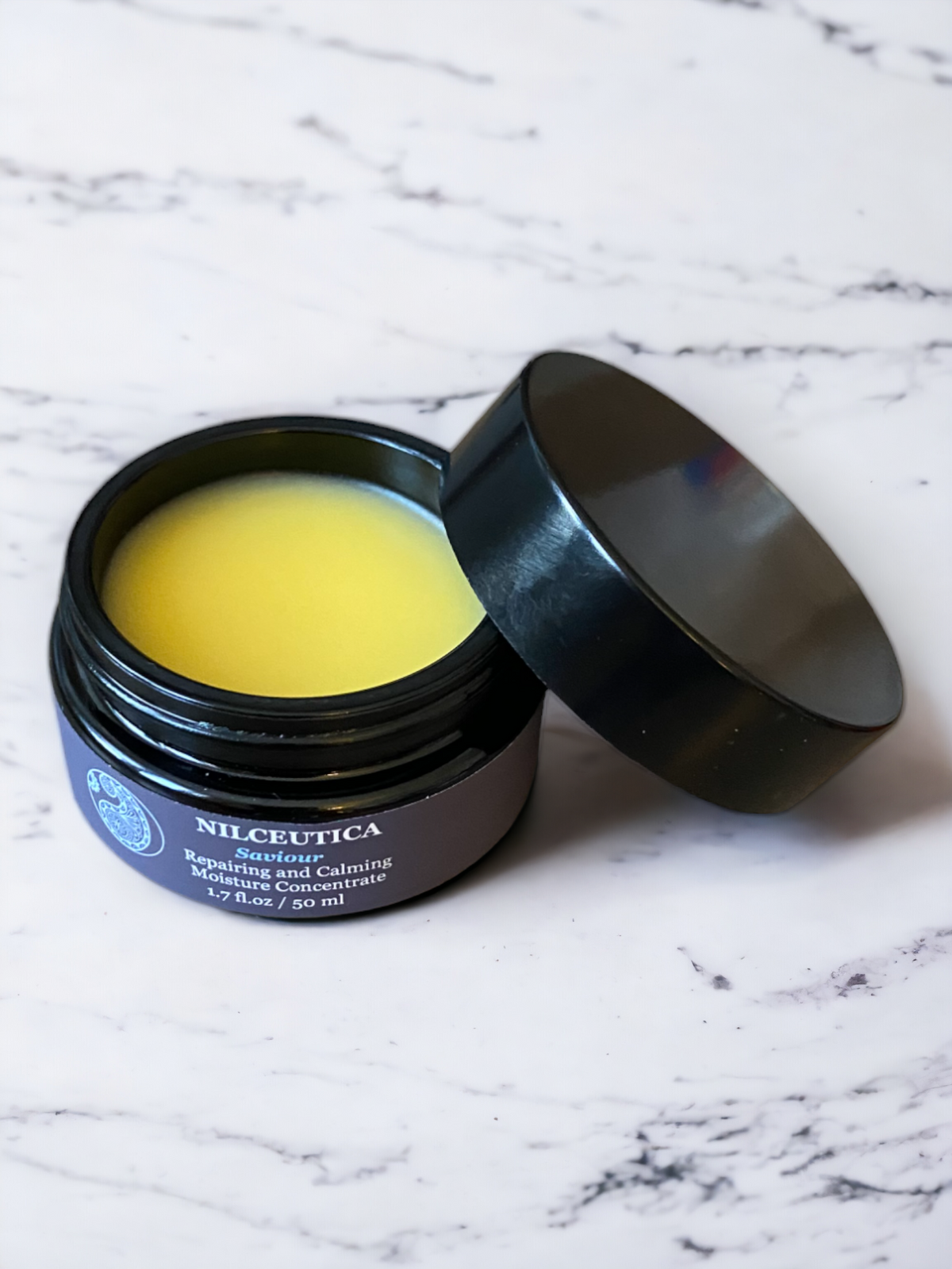 Open round jar of yellow balm beside its black lid on a white marble surface
