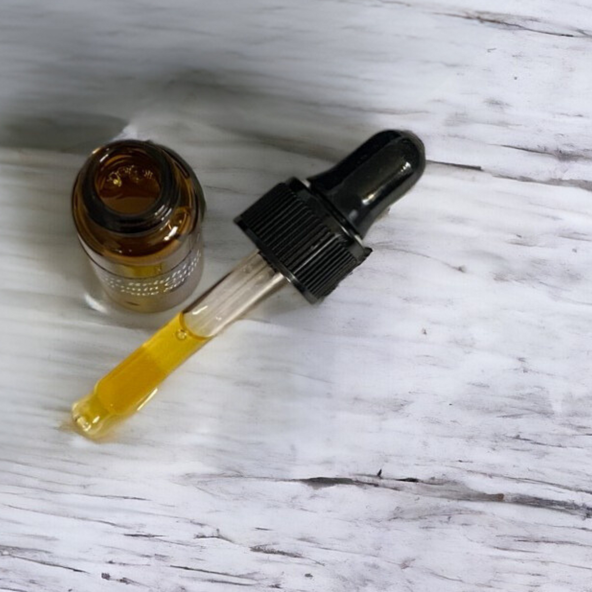 Amber vial and black dropper lying on a weathered white wood surface
