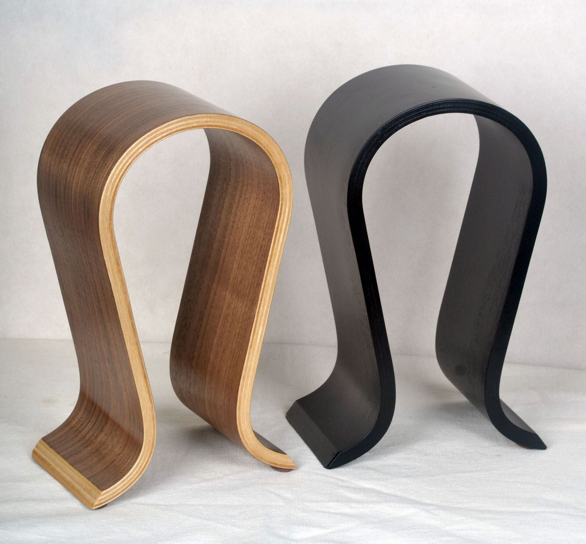 Light wood-edged walnut-look and black curved headphone stands side by side