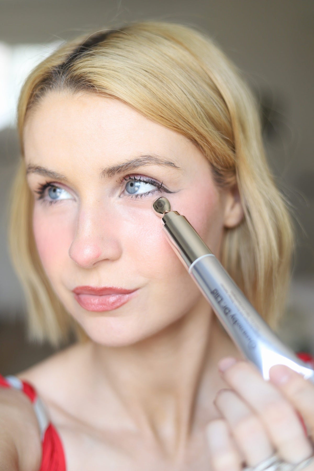 Woman with blonde hair applying the eye cream under her eye with the roller tip