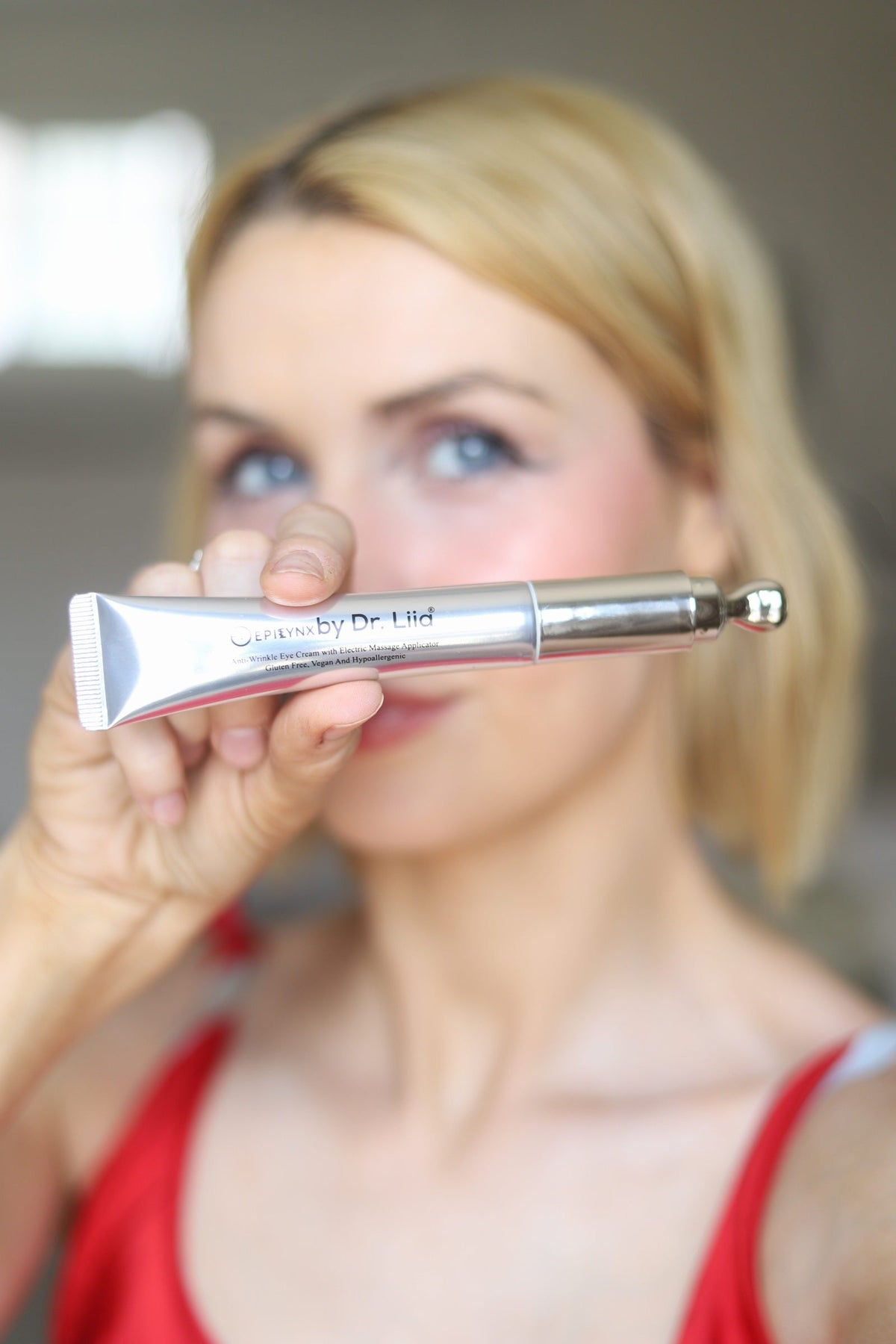 Woman in a red top holding the eye cream tube near her nose