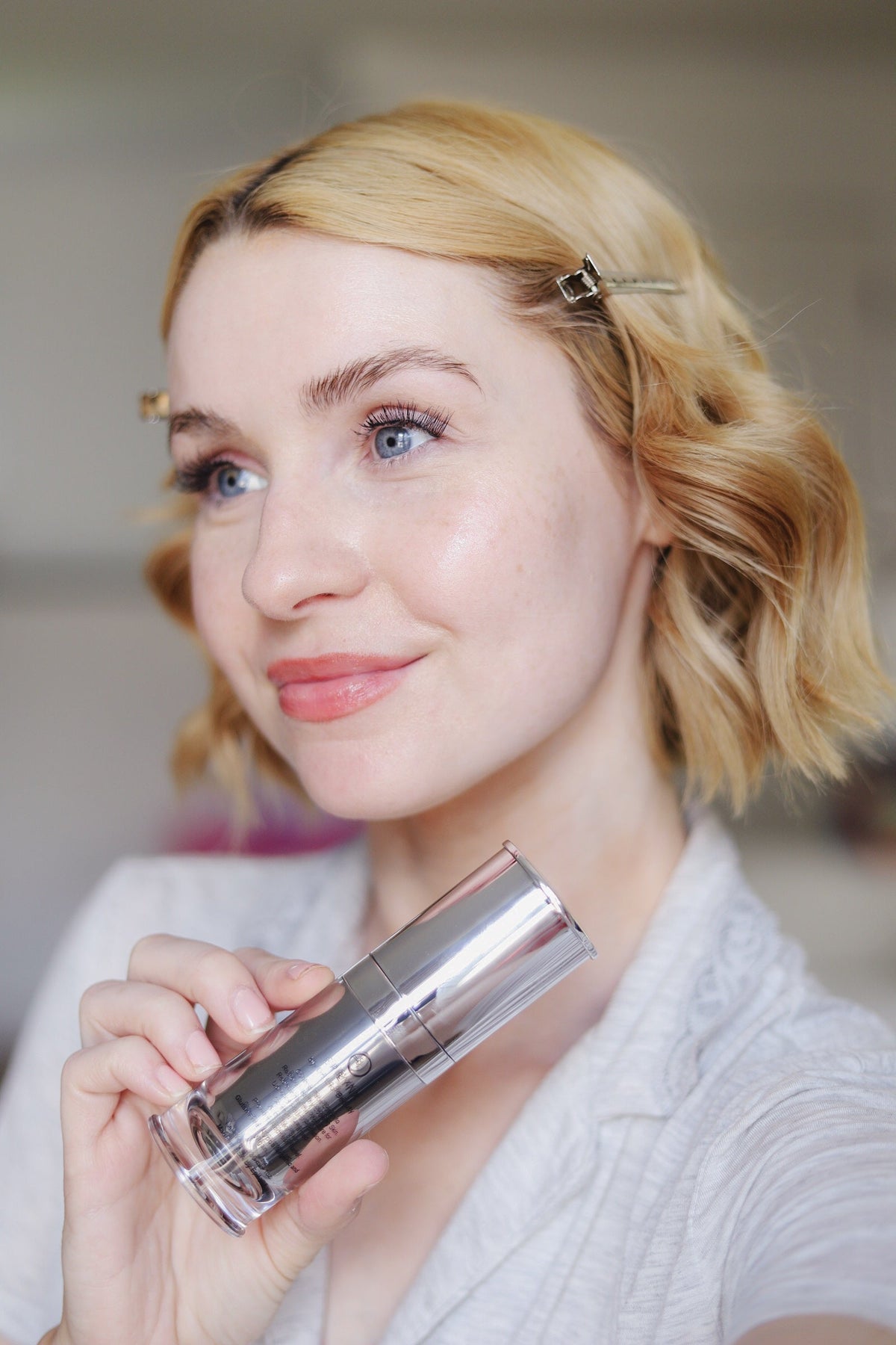 Woman with wavy blonde hair holding a small silver serum bottle
