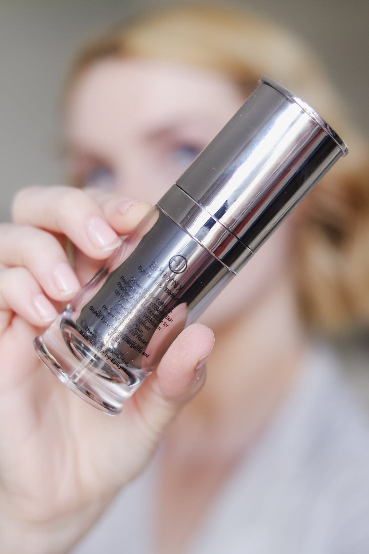 Close-up of a hand holding the silver serum bottle toward the camera
