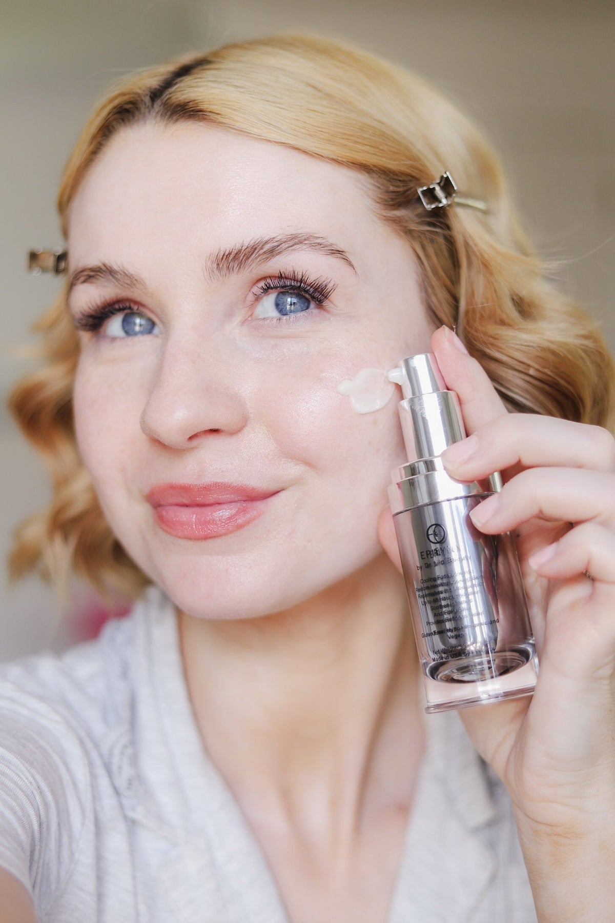Woman holding the silver serum bottle beside her cheek