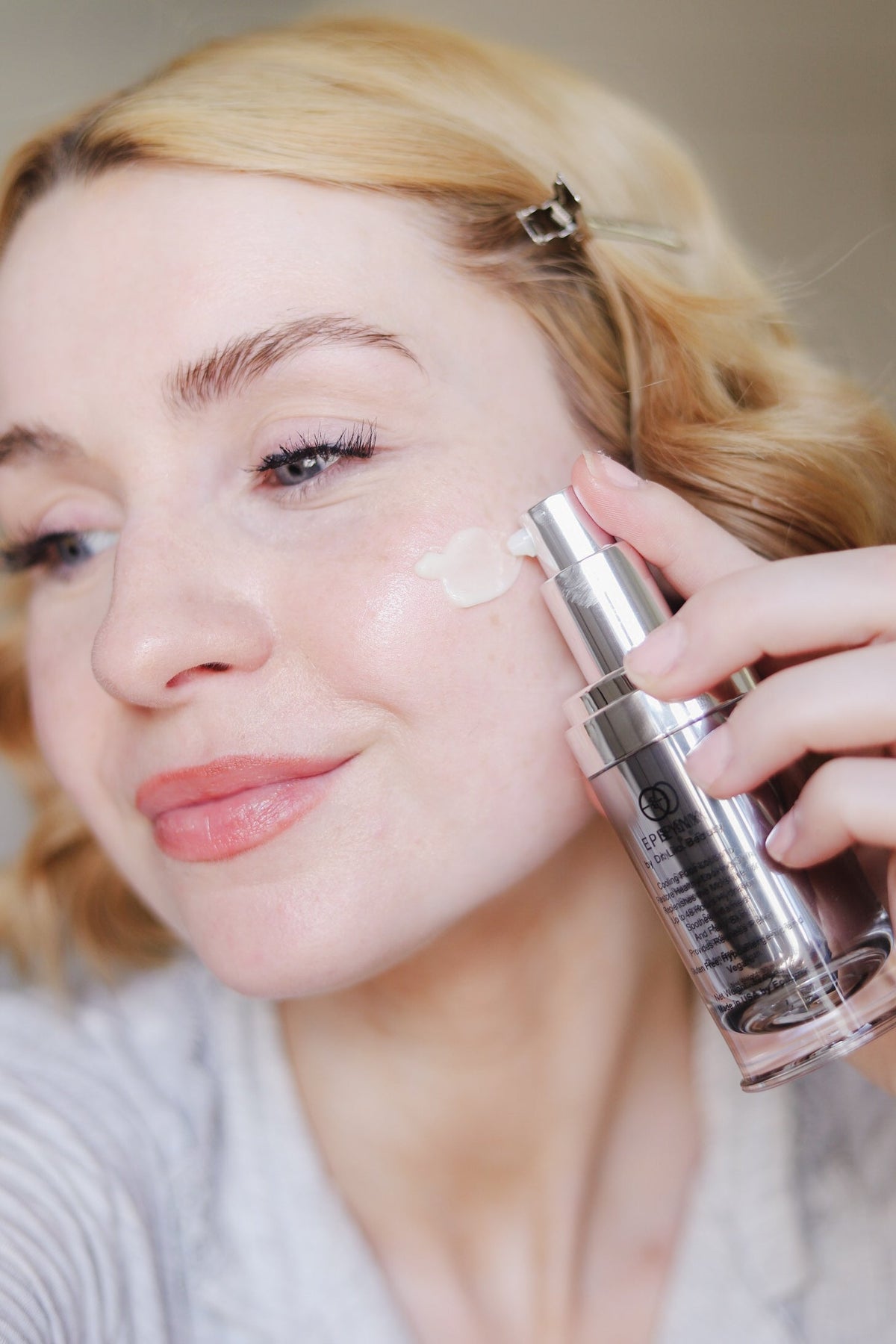 Woman with wavy blonde hair holding the serum bottle beside her face